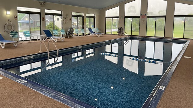 An indoor swimming pool with clear markings, lounge chairs, and large windows offering views of the outdoors. - Travelodge by Wyndham Hershey (Hershey)