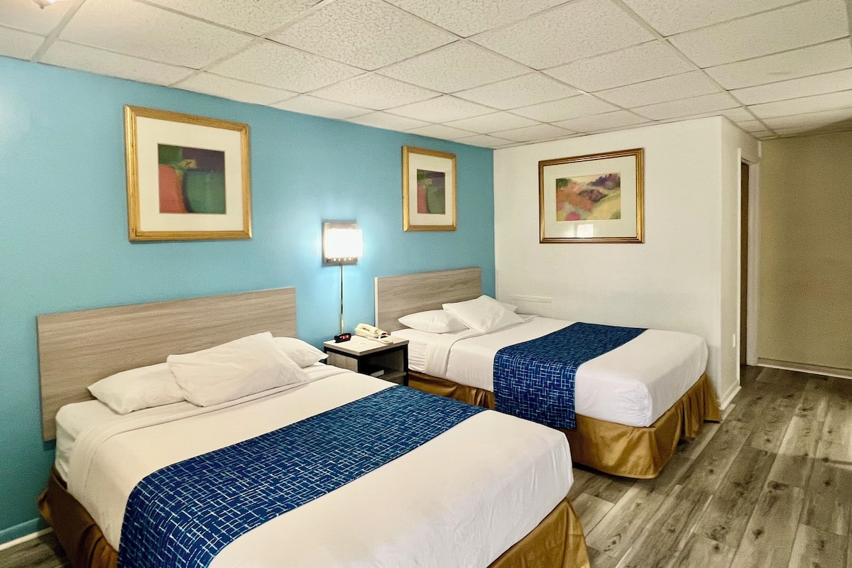 Una habitación de hotel con dos camas, una mesita de noche, una lámpara y cuadros en las paredes.