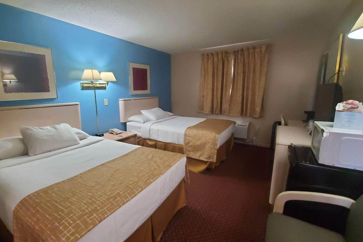 Habitación de hotel con dos camas, un escritorio, una silla, un microondas y una ventana con cortinas.