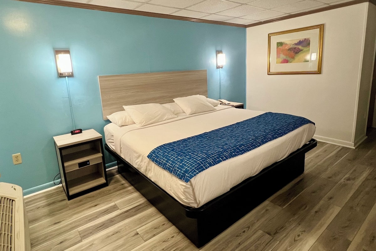 Una habitación de hotel con una cama, una mesita de noche, una lámpara de pared y un cuadro.