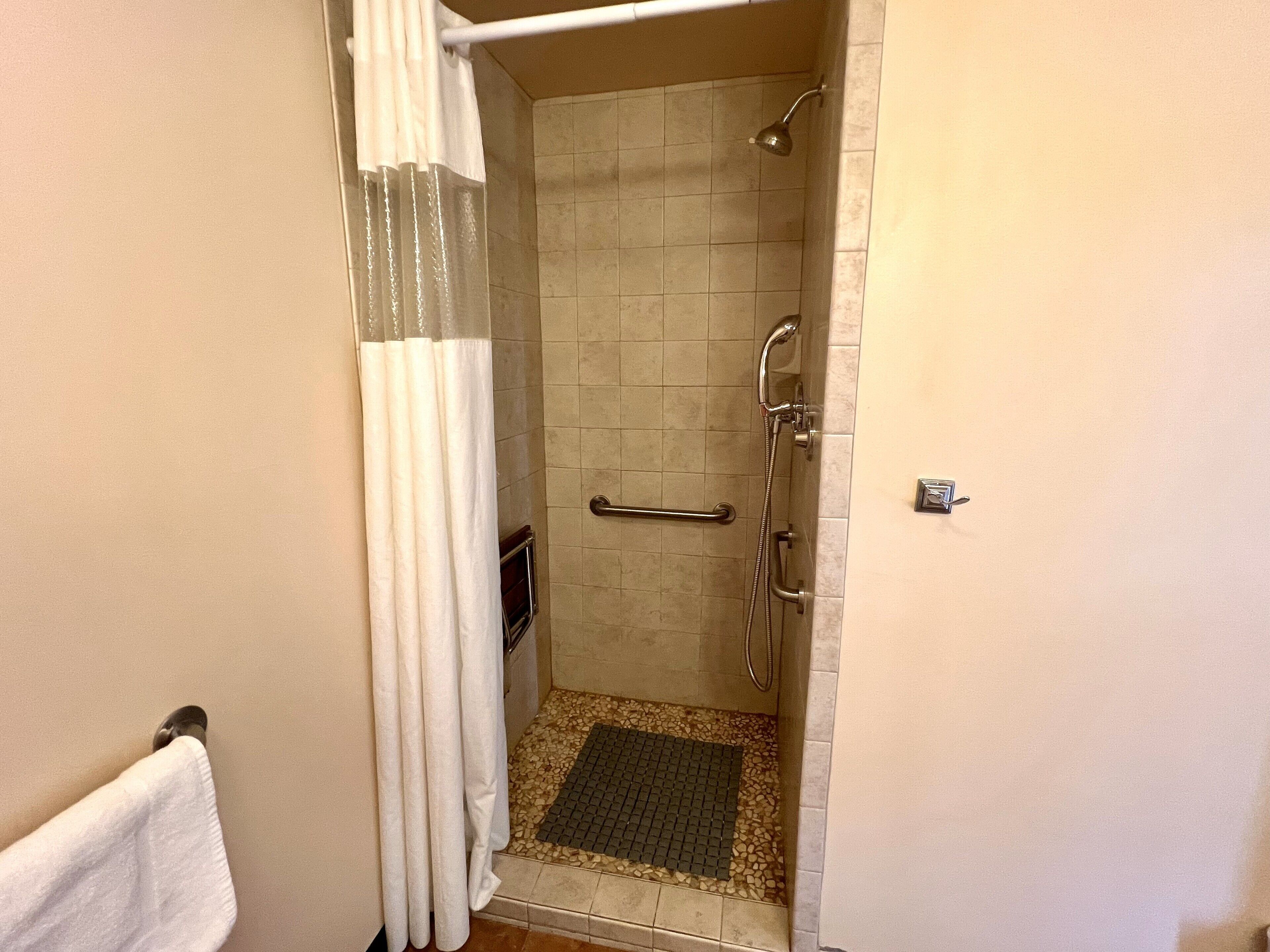 A shower with a handheld showerhead, a grab bar, and a tiled floor.