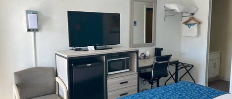 A hotel room with a bed, a desk with a computer, a television, a microwave, and a chair.