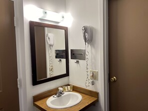 Un baño con un lavamanos blanco, un espejo, un secador de pelo y una estación de carga para secador.