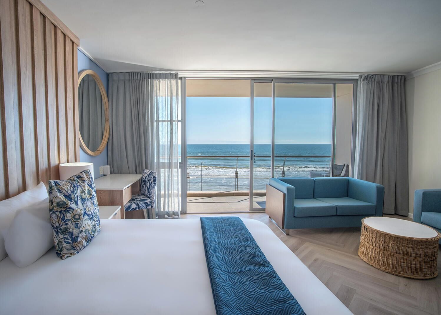 A hotel room with a bed, a desk, a chair, a sofa, and a view of the ocean.