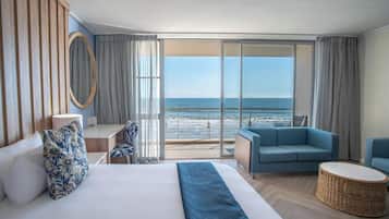 Una camera d'albergo con un letto, una scrivania, una sedia, un divano e vista sull'oceano.