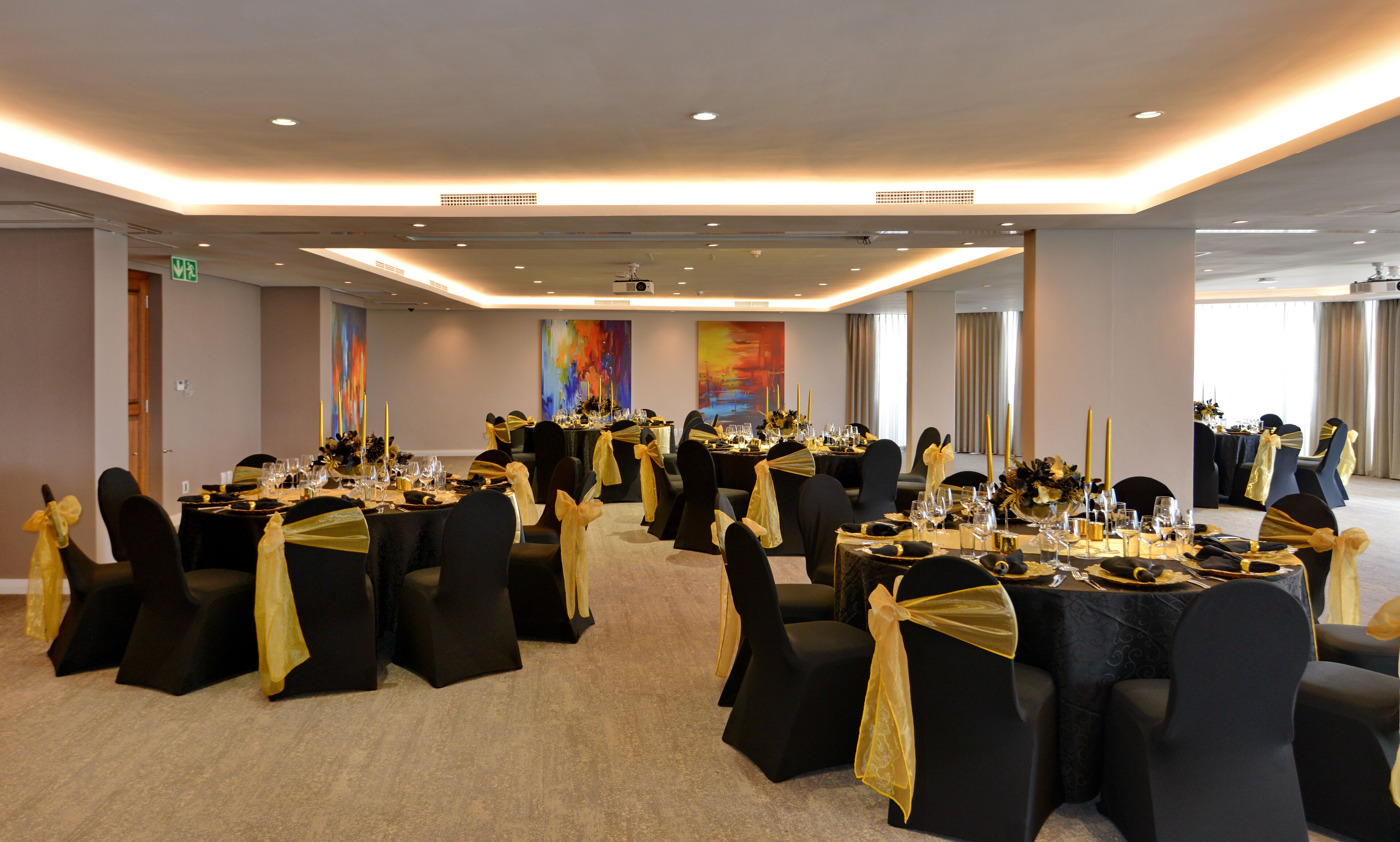 A banquet hall with round tables, black chairs with yellow sashes, and a carpeted floor.