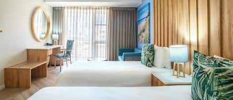 Habitación de hotel con dos camas, un escritorio, una silla, un espejo redondo y un ventanal con cortinas.