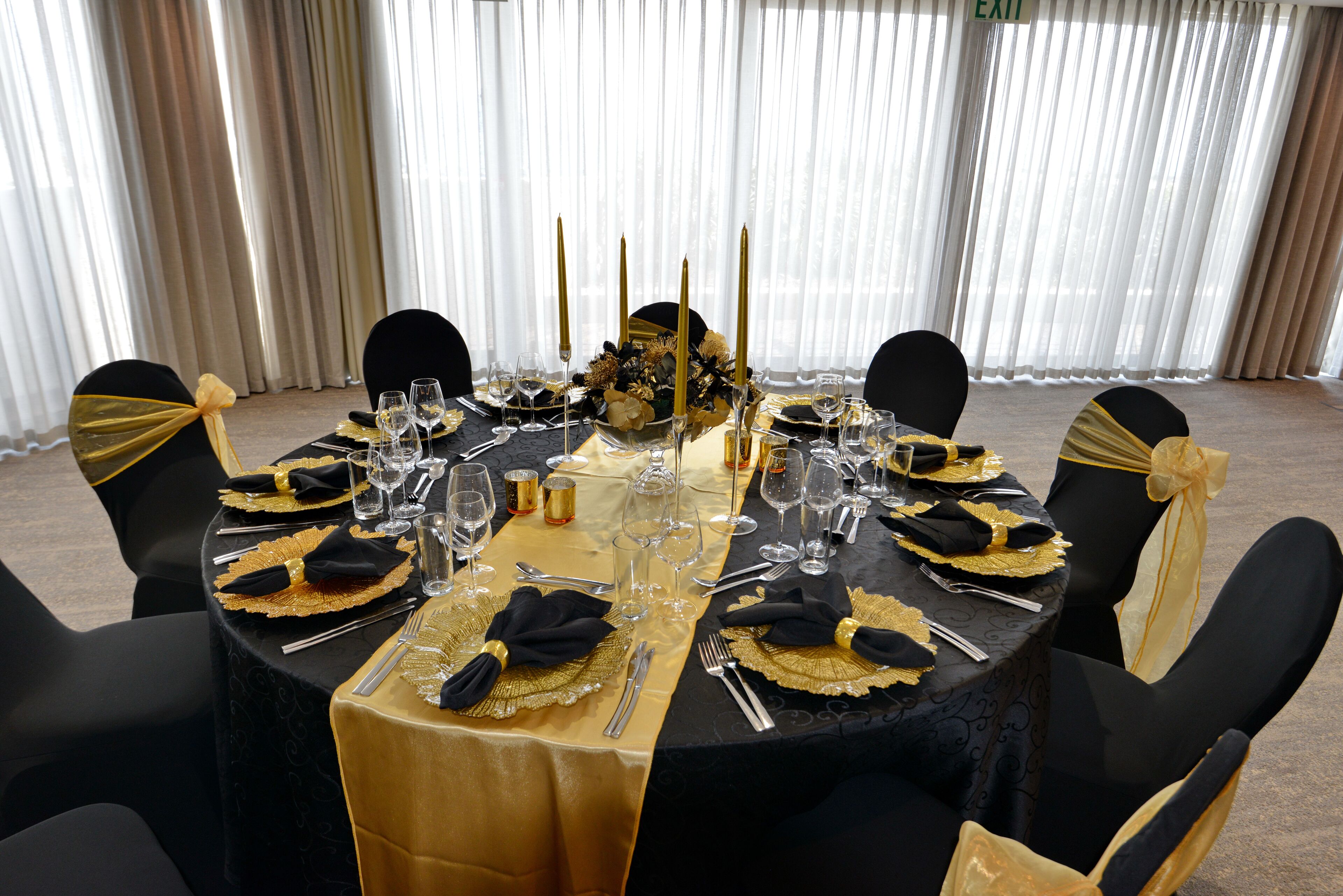 Een ronde tafel gedekt voor een formeel evenement, met een zwart-gouden tafelkleed, gouden servetten en kandelaars.