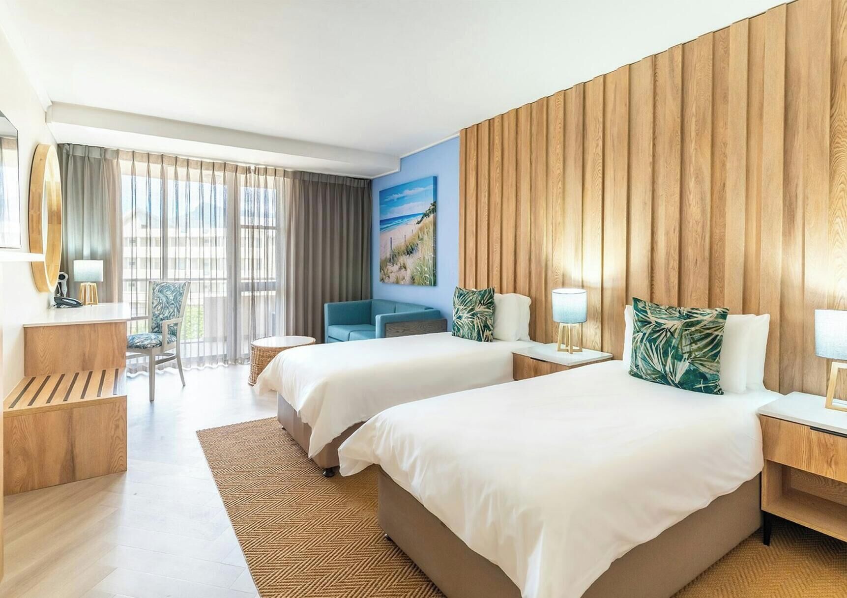 Een hotelkamer met twee bedden, een bureau, een stoel en een groot raam met gordijnen.