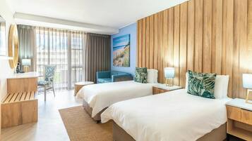 Ein Hotelzimmer mit zwei Betten, einem Schreibtisch, einem Stuhl und einem großen Fenster mit Vorhängen.