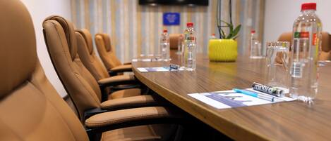 A conference room with leather chairs, a wooden table, water bottles, and a TV on the wall.