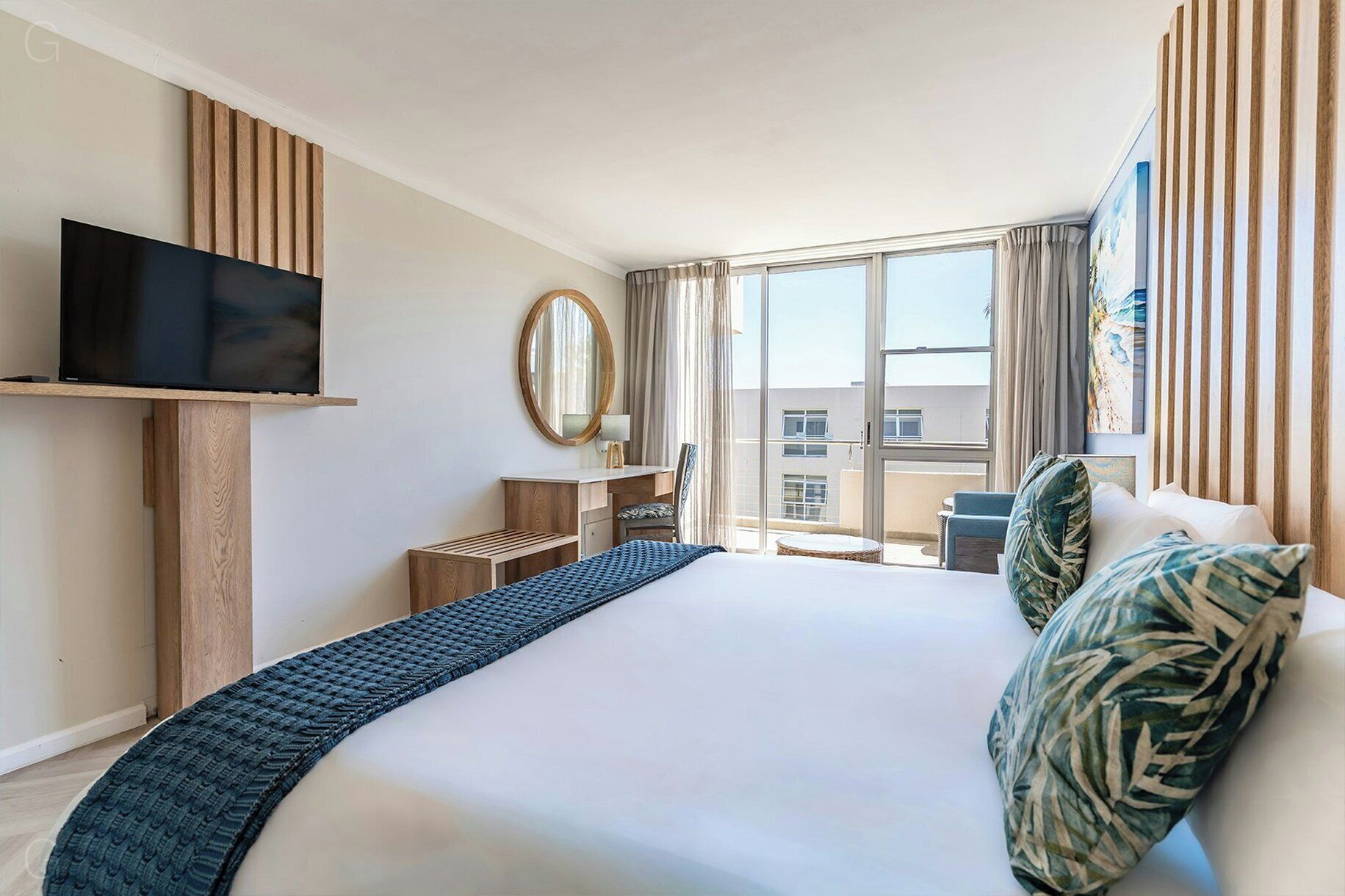 Een hotelkamer met een groot bed, een flatscreen televisie, een bureau met stoel, een raam met gordijnen en uitzicht op gebouwen.