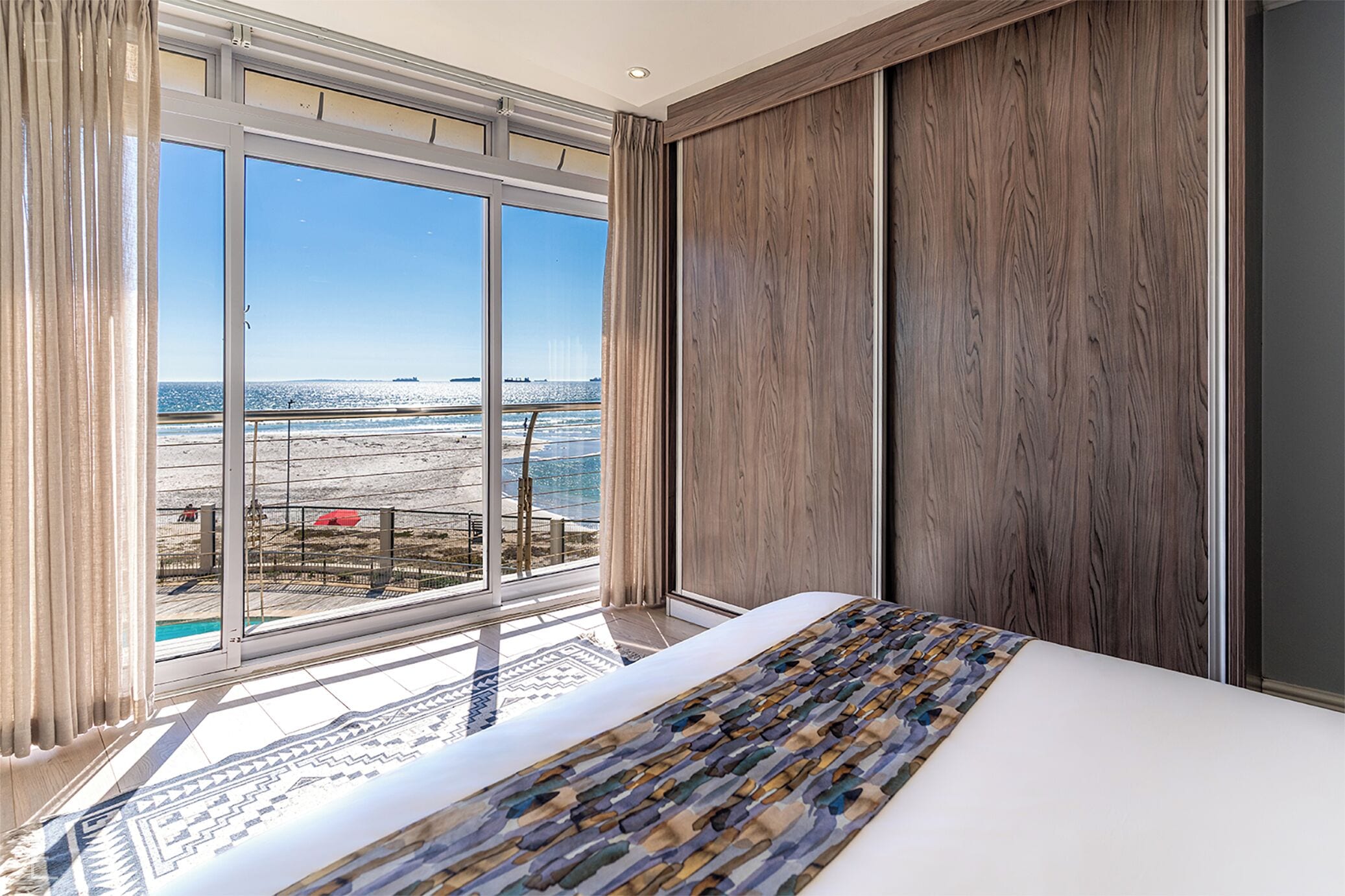 A hotel room with a large window, a bed with a patterned bedspread, and wooden paneling on the walls.