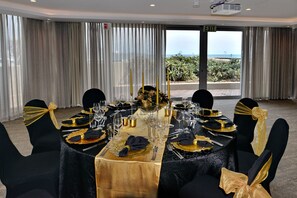 A banquet table set for a formal event with a view of the sea through large windows.