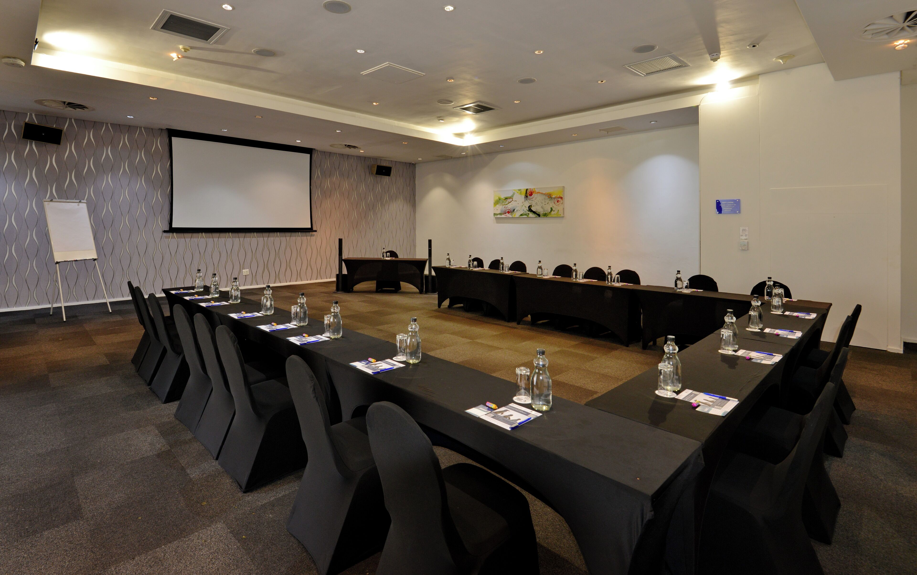 A conference room with a long table, chairs, a projector screen, and a whiteboard.
