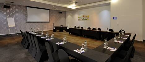 A conference room with a long table, chairs, a projector screen, and a whiteboard.