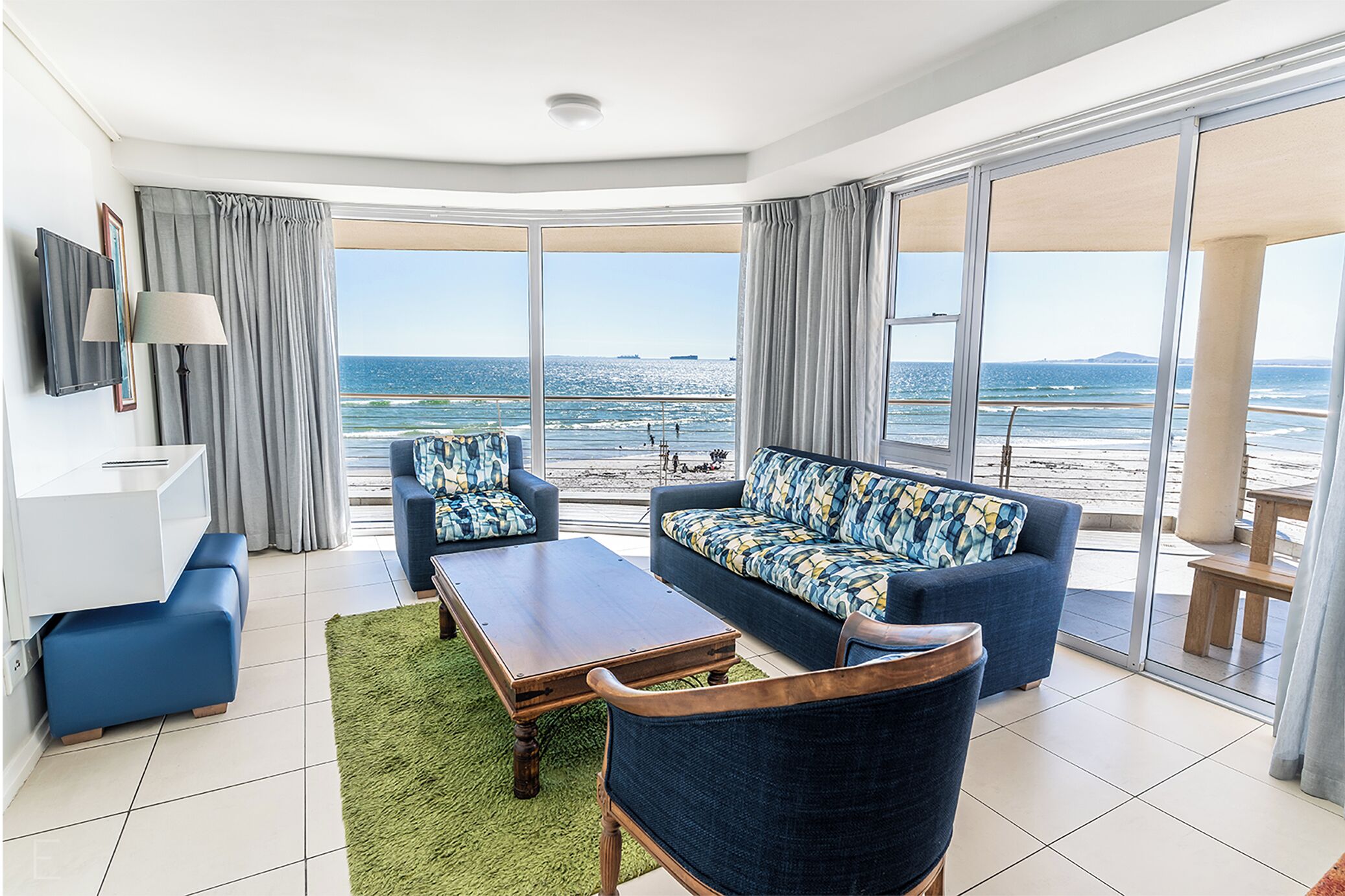 Ein modernes Wohnzimmer mit Sofa, Sessel, Couchtisch und Blick aufs Meer.