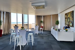 A modern hotel room with large windows, a bar area, and several white bar stools.