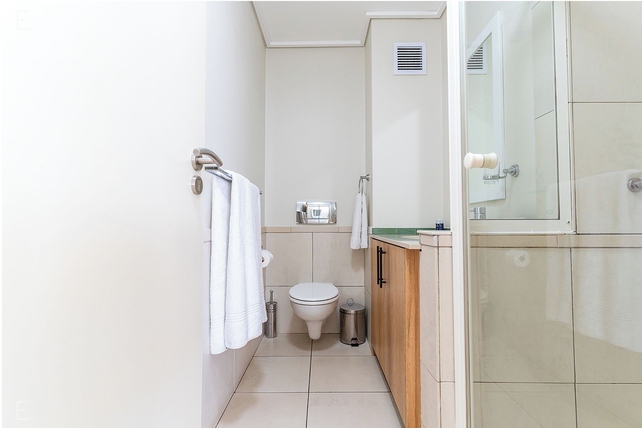 A bathroom with a toilet, a trash bin, a towel rack, and a mirror.