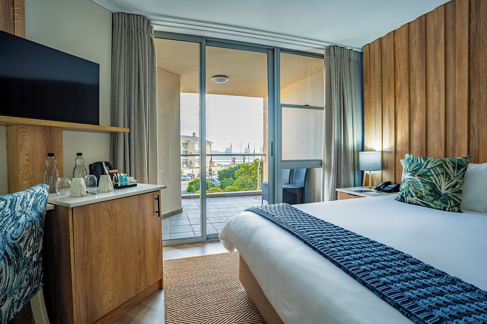 Habitación de hotel con cama, escritorio, televisión, balcón y vistas, además de una ventana.