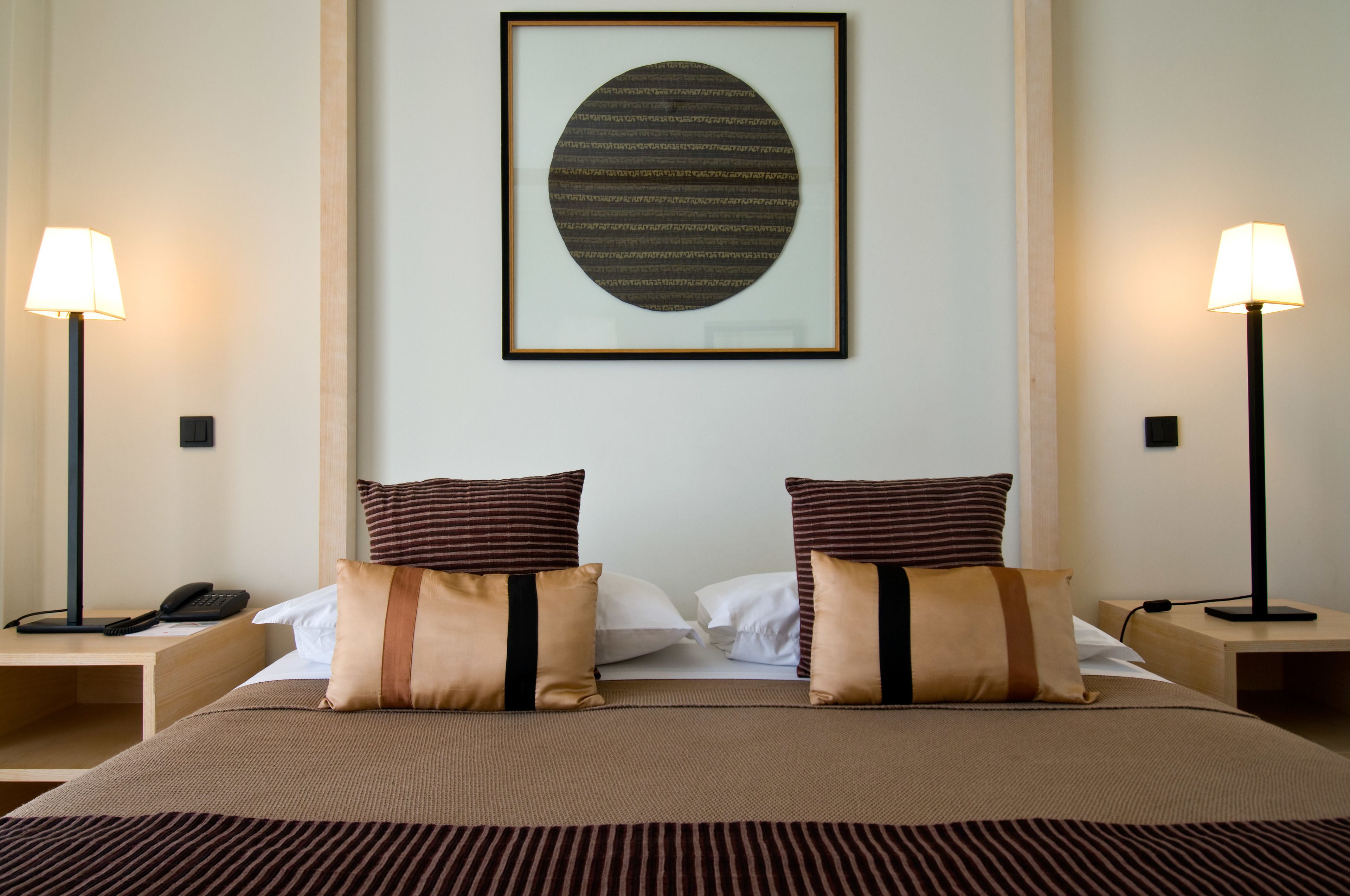 Une chambre d’hôtel avec un grand lit, deux tables de chevet, une œuvre d’art encadrée au mur et deux lampadaires.