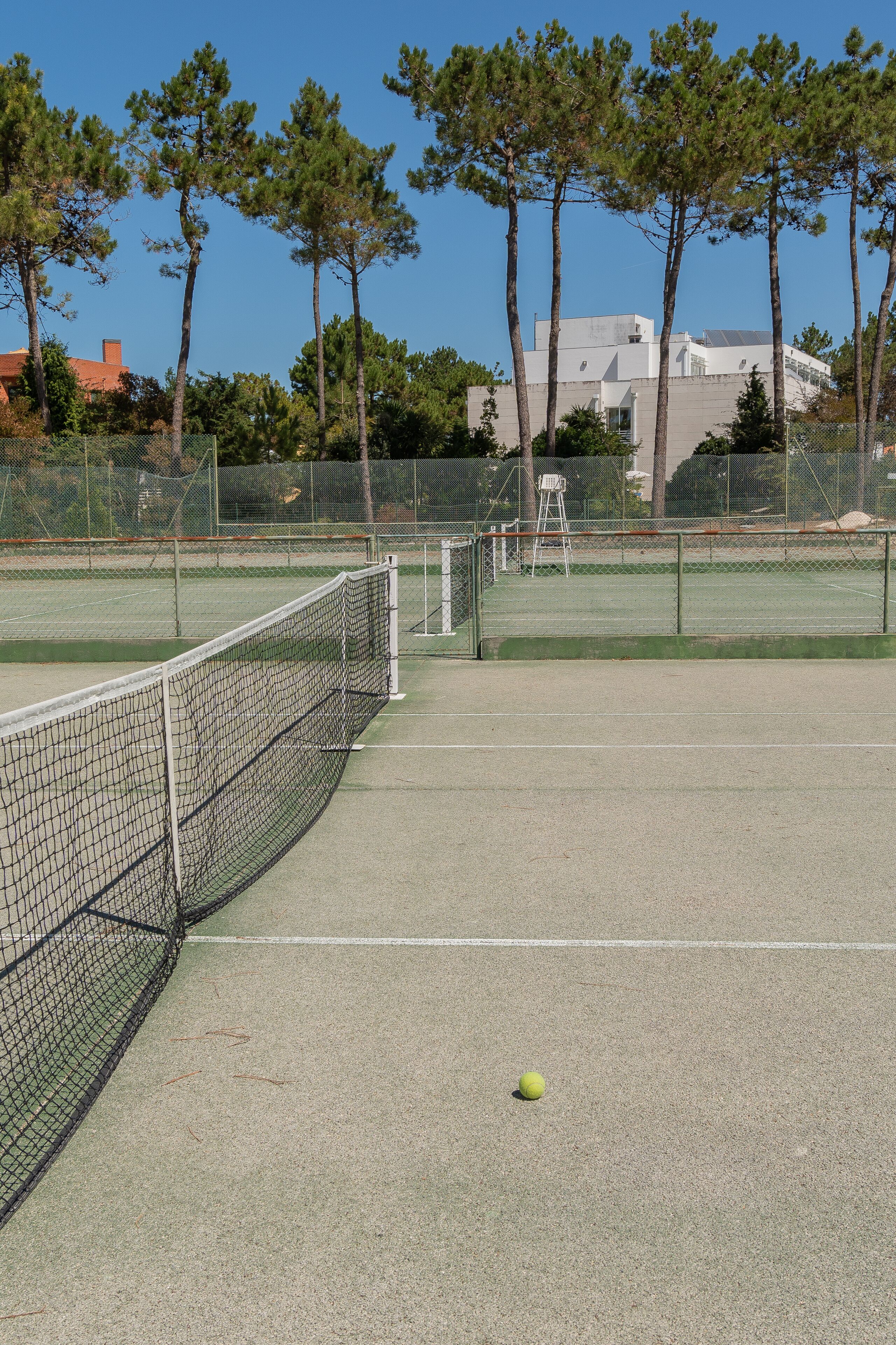 A tennis court with a net, trees, and a building in the background.