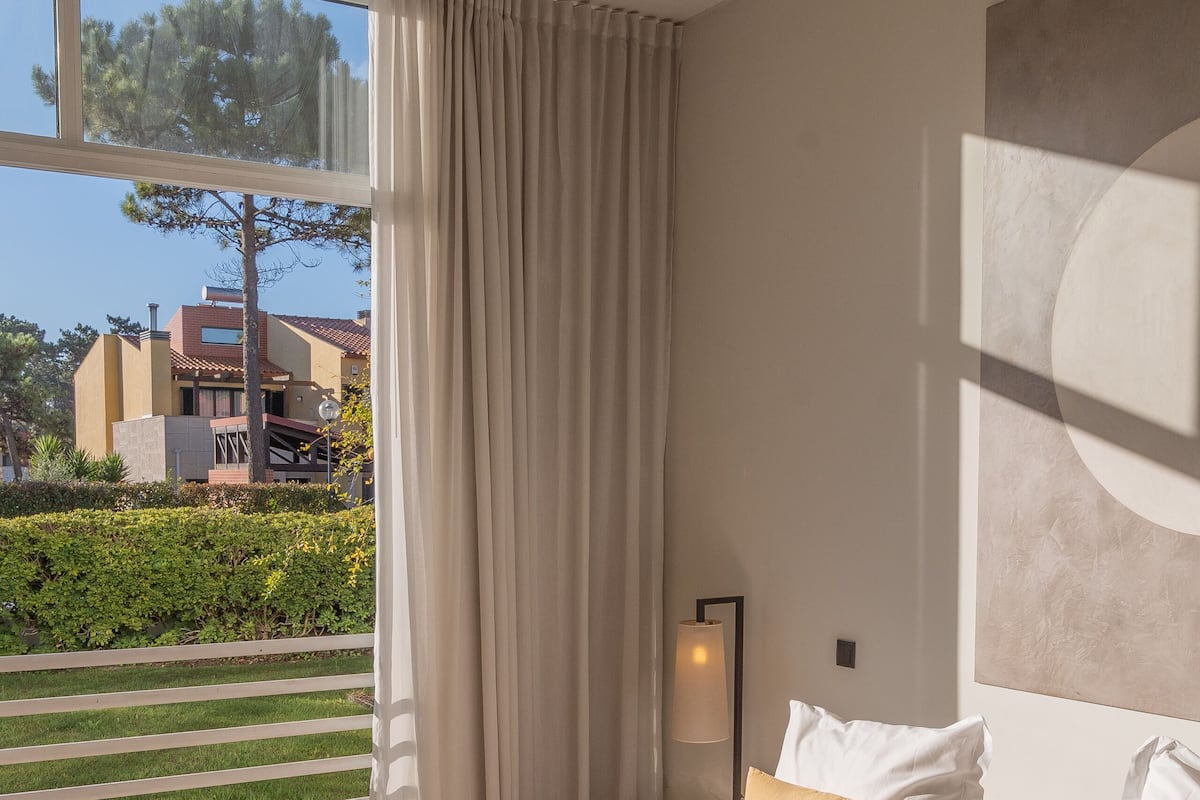 A modern hotel room with a large bed, a view of the outdoors, and a minimalist decor.