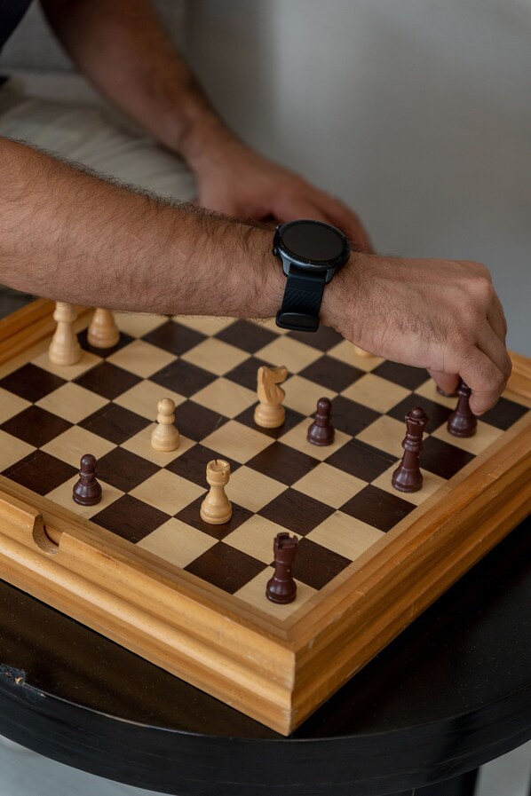 Un tablero de ajedrez con piezas sobre él, un reloj de pulsera en la muñeca de una persona, y una mesa de madera.