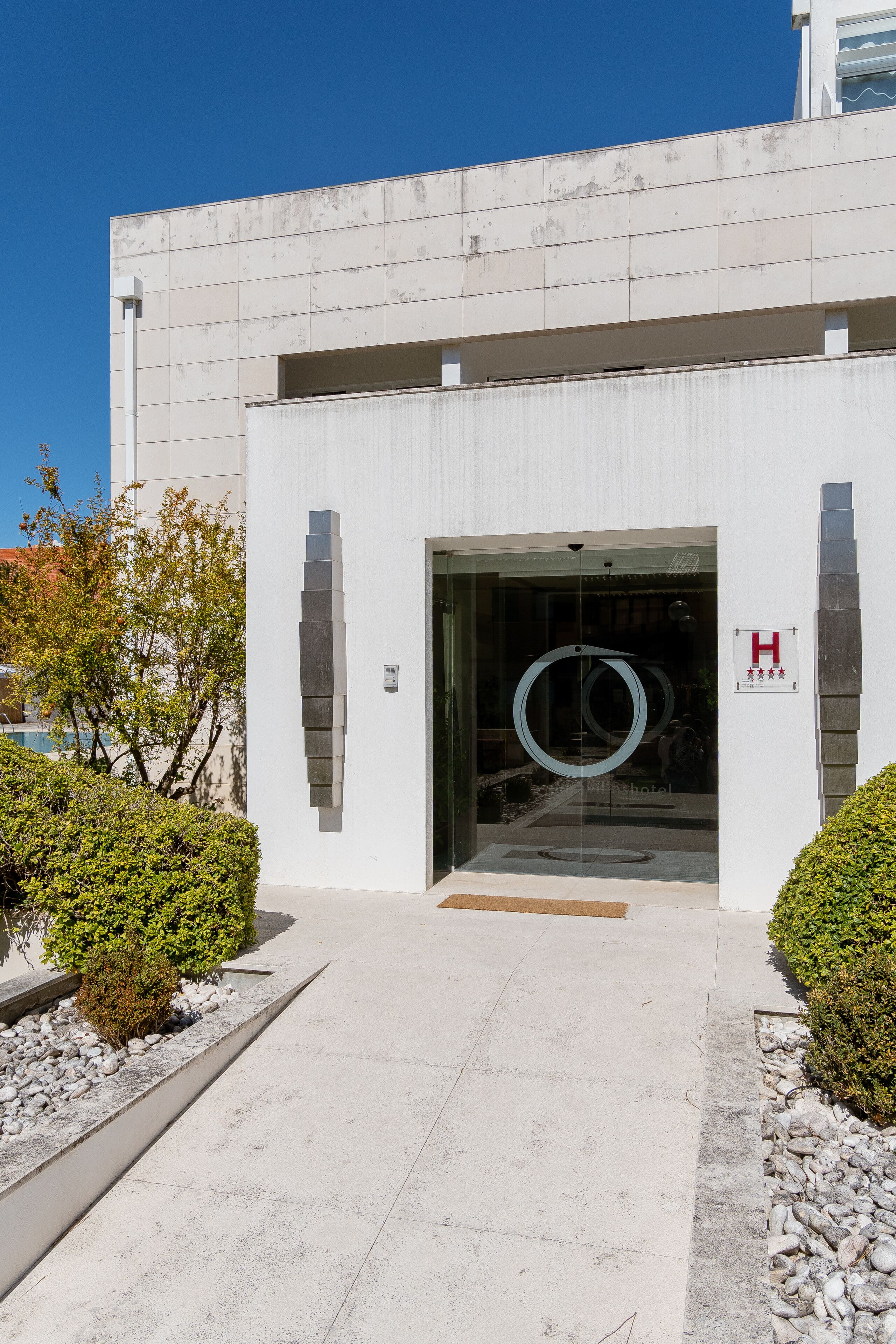 A modern building entrance with a glass door, a logo, and a clear sky.