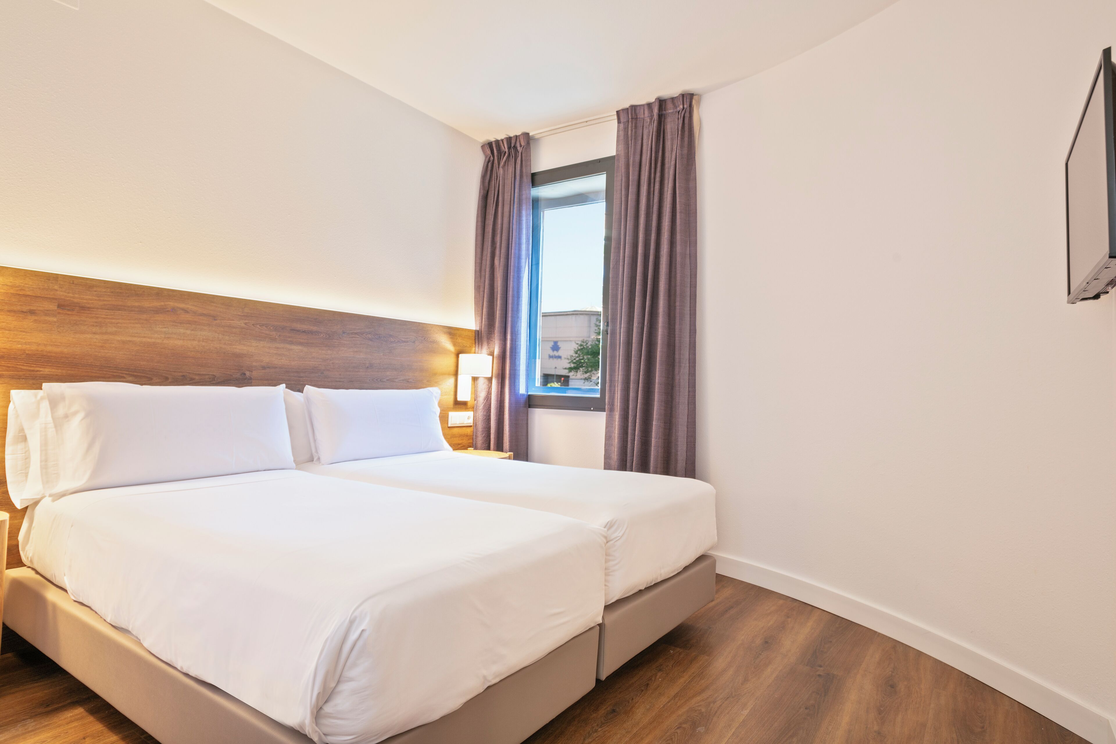 A double bed with white linens, a wooden headboard, and a nightstand with a lamp.