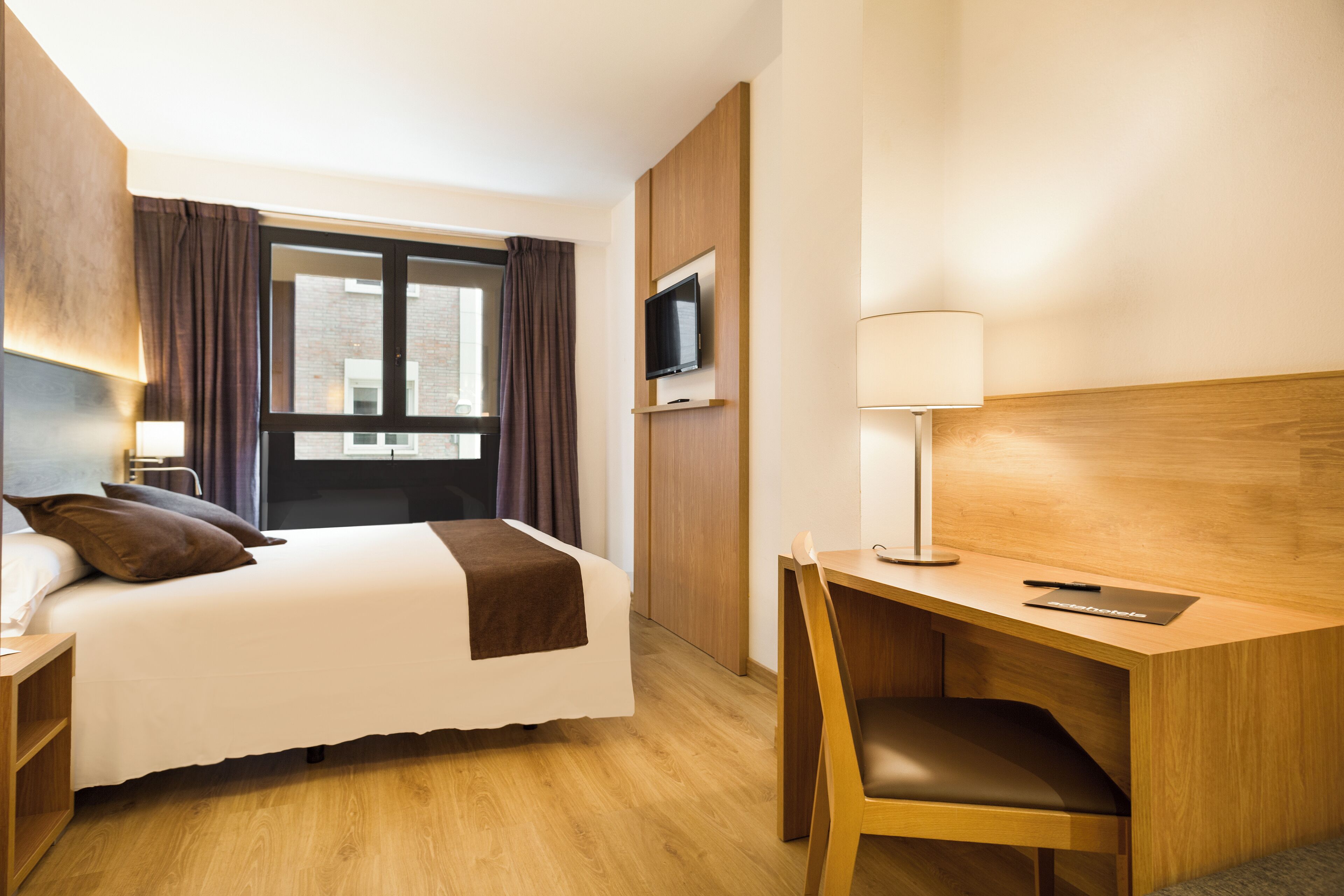 Ein Hotelzimmer mit Bett, Schreibtisch, Stuhl, Fernseher und Vorhängen.