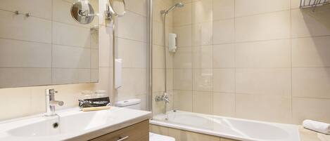 A modern bathroom with a large mirror, a bathtub, a toilet, and a vanity with a sink.