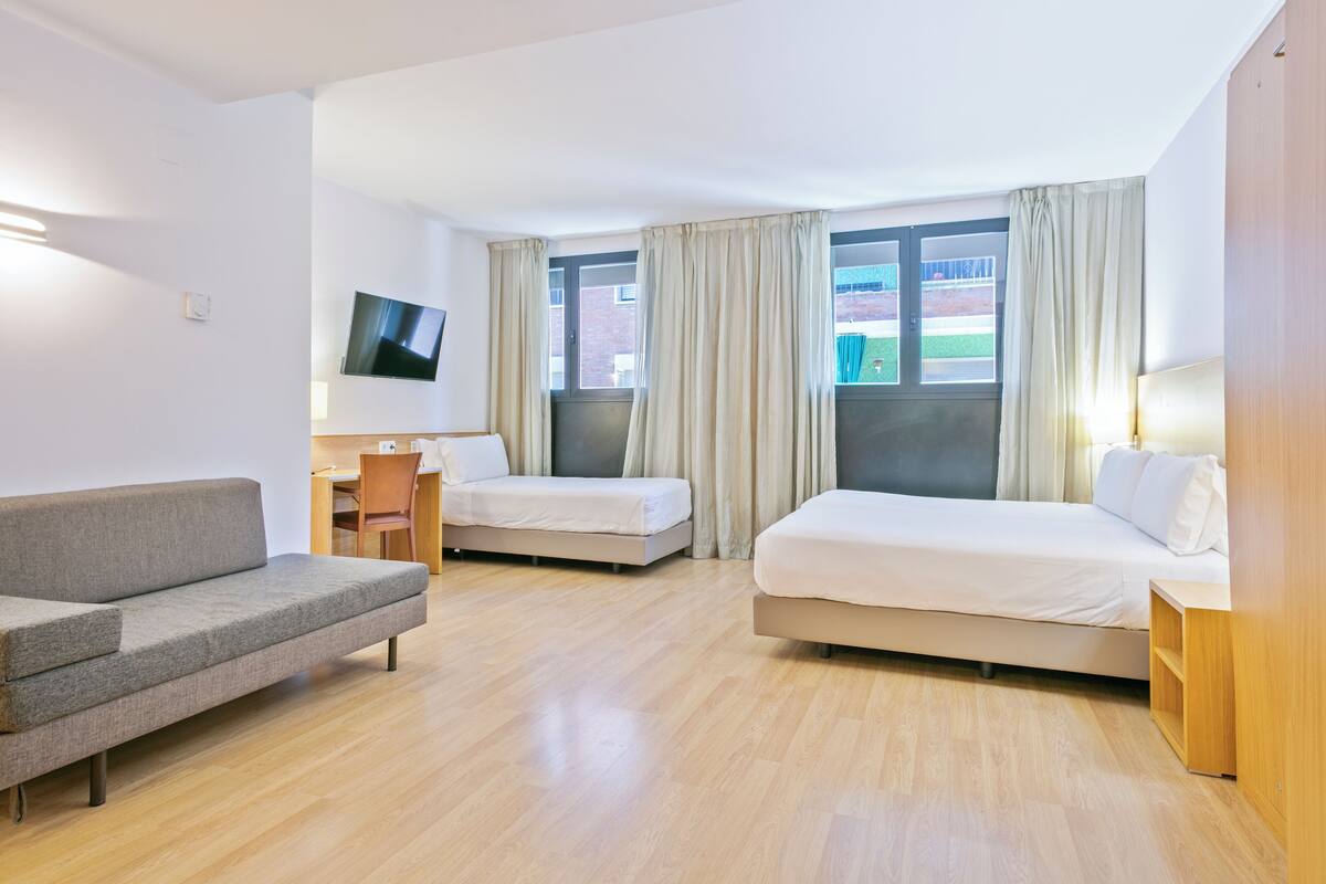 Habitación de hotel con dos camas, un sofá, un escritorio y un televisor.