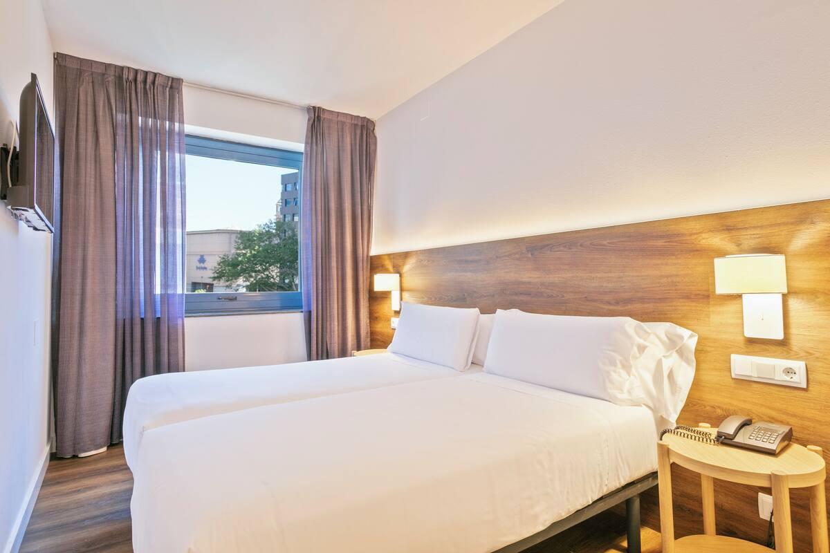 Una habitación de hotel con una cama grande, una mesita de noche con teléfono y una ventana con cortinas.