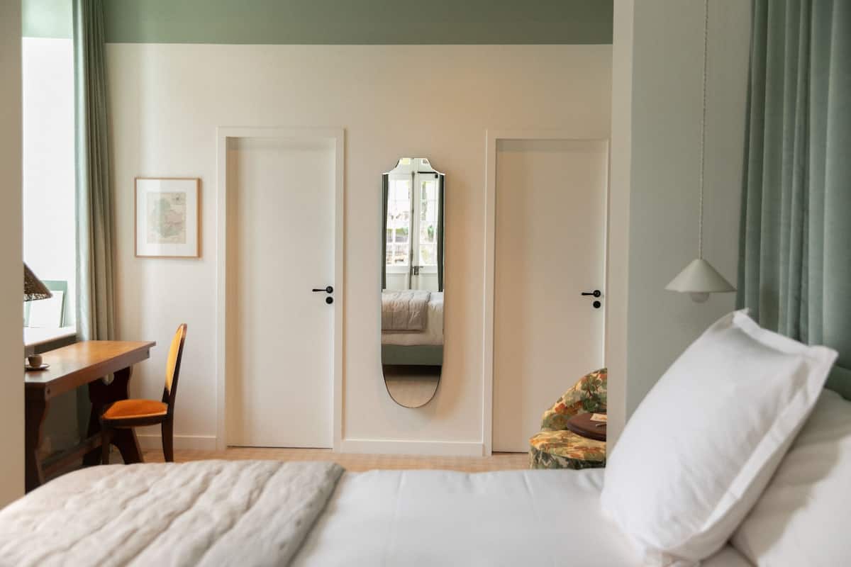 A bedroom with a bed, a desk, a chair, and a door with a mirror.