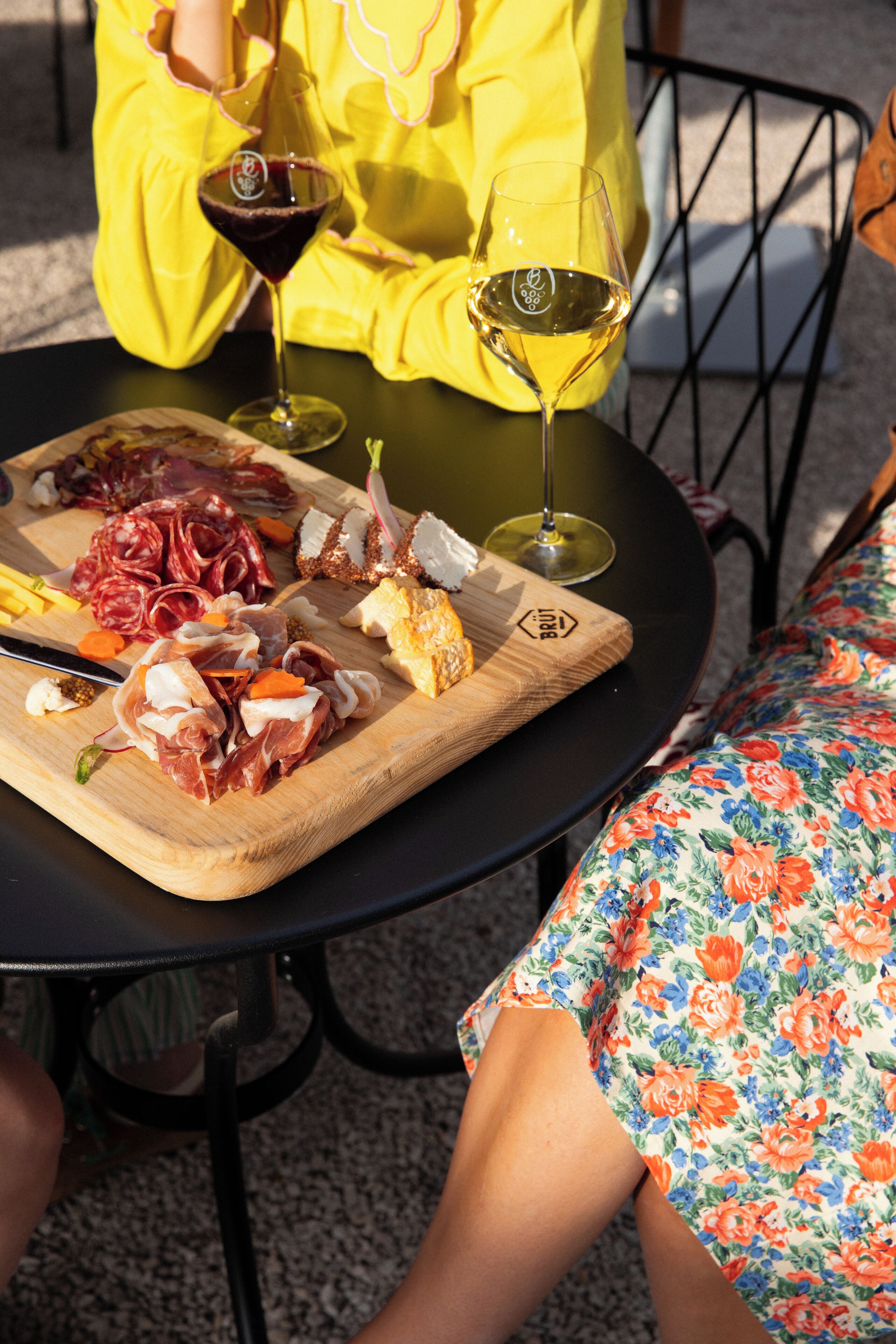 A table with a charcuterie board, two glasses of wine, and a person in a yellow shirt.