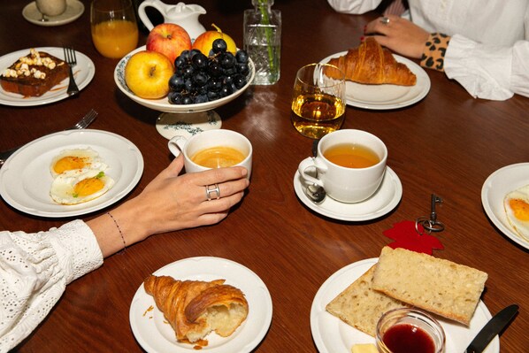 Una mesa de comedor con platos de comida, incluyendo cruasanes, pan y un bol de fruta.