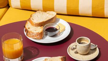 A breakfast setting with toast, butter, jam, coffee, and orange juice on a table with a yellow-striped cushion in the background.
