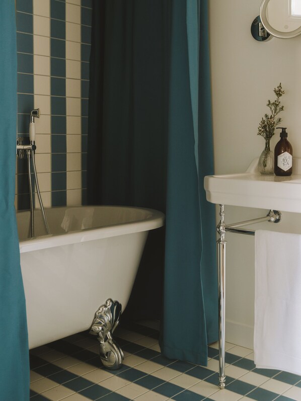 A bathroom with a freestanding bathtub, a white sink, a mirror, and a shower head.