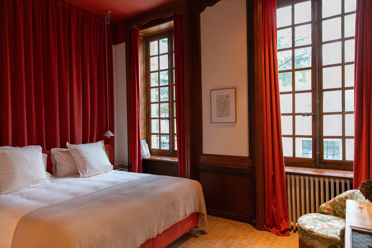 A room with a large bed, red curtains, and a window with a view of trees.