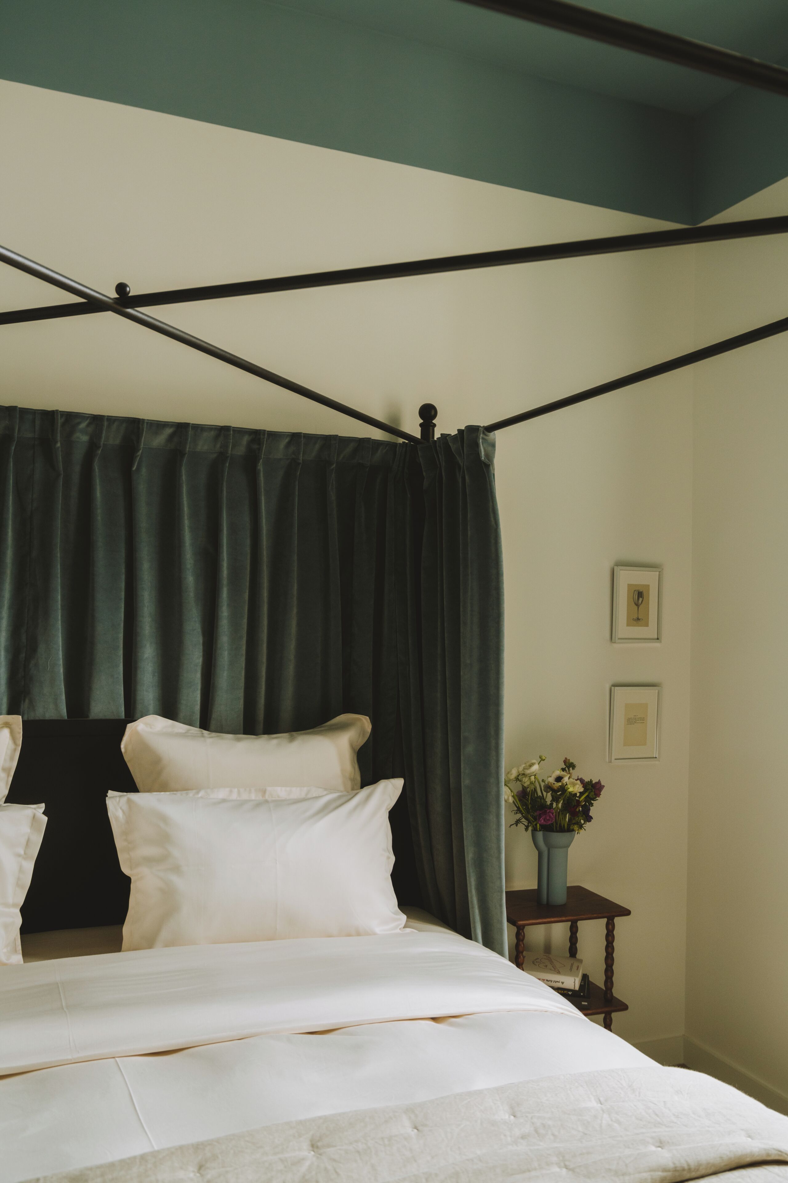 A four-poster bed with white linens and a dark green canopy.