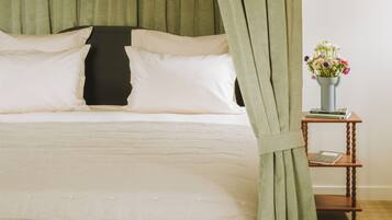 Una cama con cortinas verdes, un cabecero de madera y una mesita con un florero.