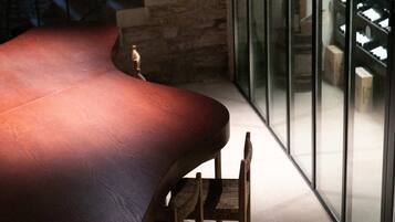 A modern interior with a curved wooden table and chairs, a stone wall, and a staircase with glass railings.