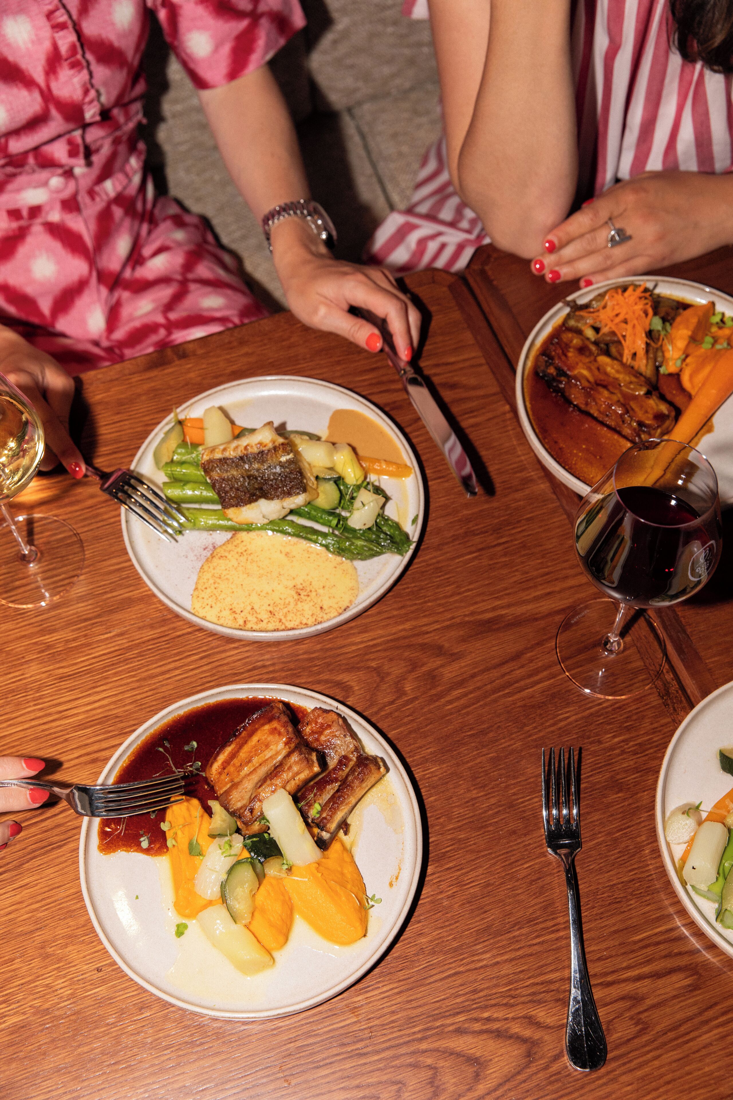 A wooden dining table with plates of food, forks, and wine glasses.