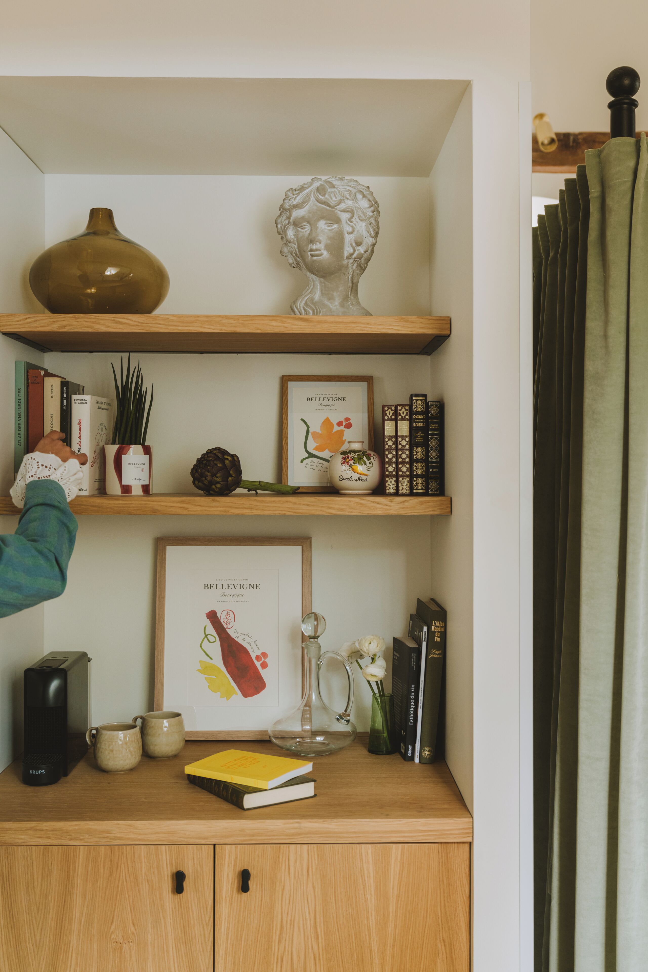 Una estantería de madera con libros, un florero y un cuadro enmarcado.