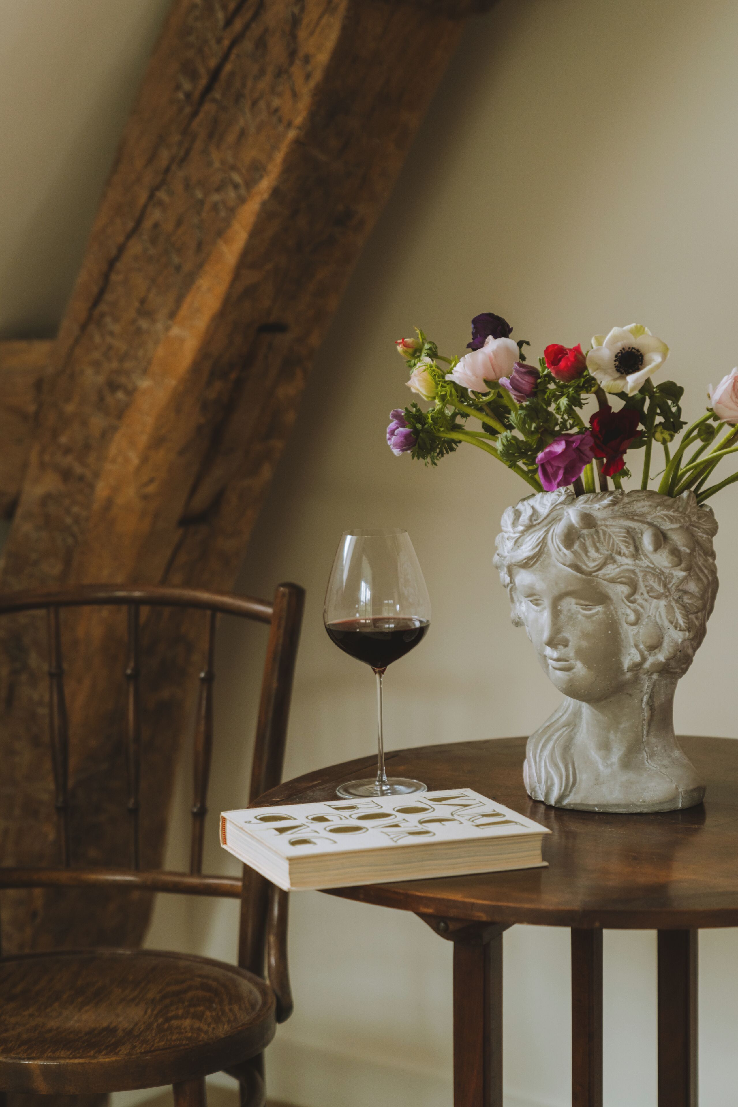 A wooden table with a vase of flowers, a wine glass, and a book.