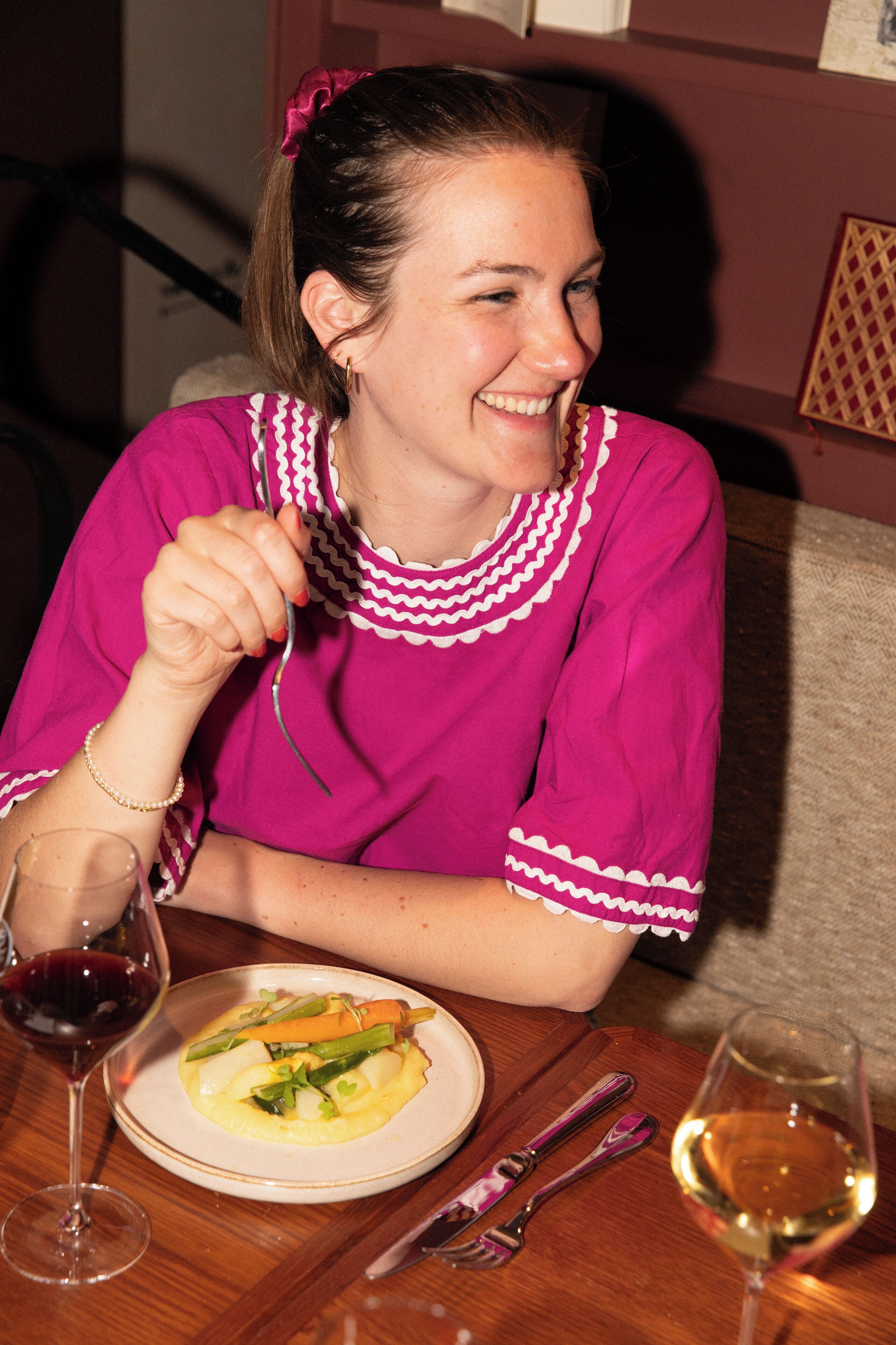 A person seated at a table with a plate of food, a wine glass, and cutlery.