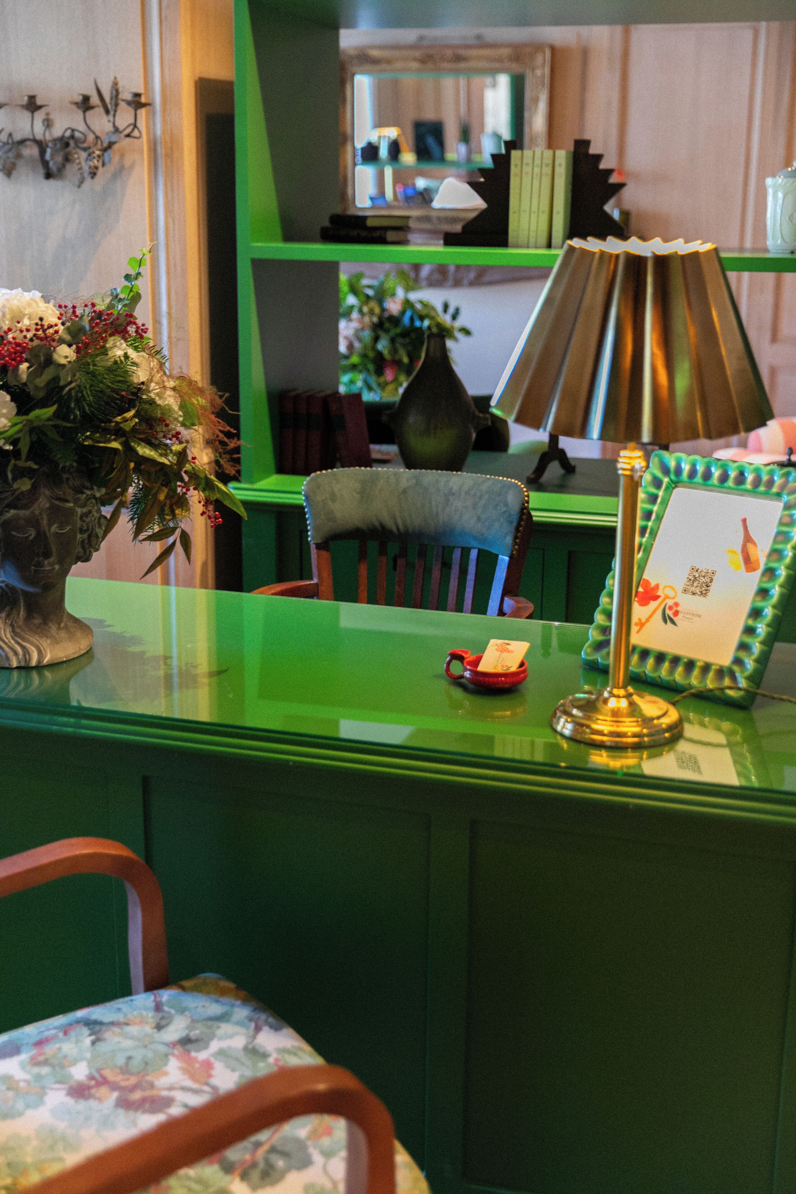 A green desk with a vase of flowers, a framed picture, and a lamp.