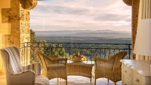 Un balcón con sillas de mimbre, una mesa con frutero y vistas a las montañas.
