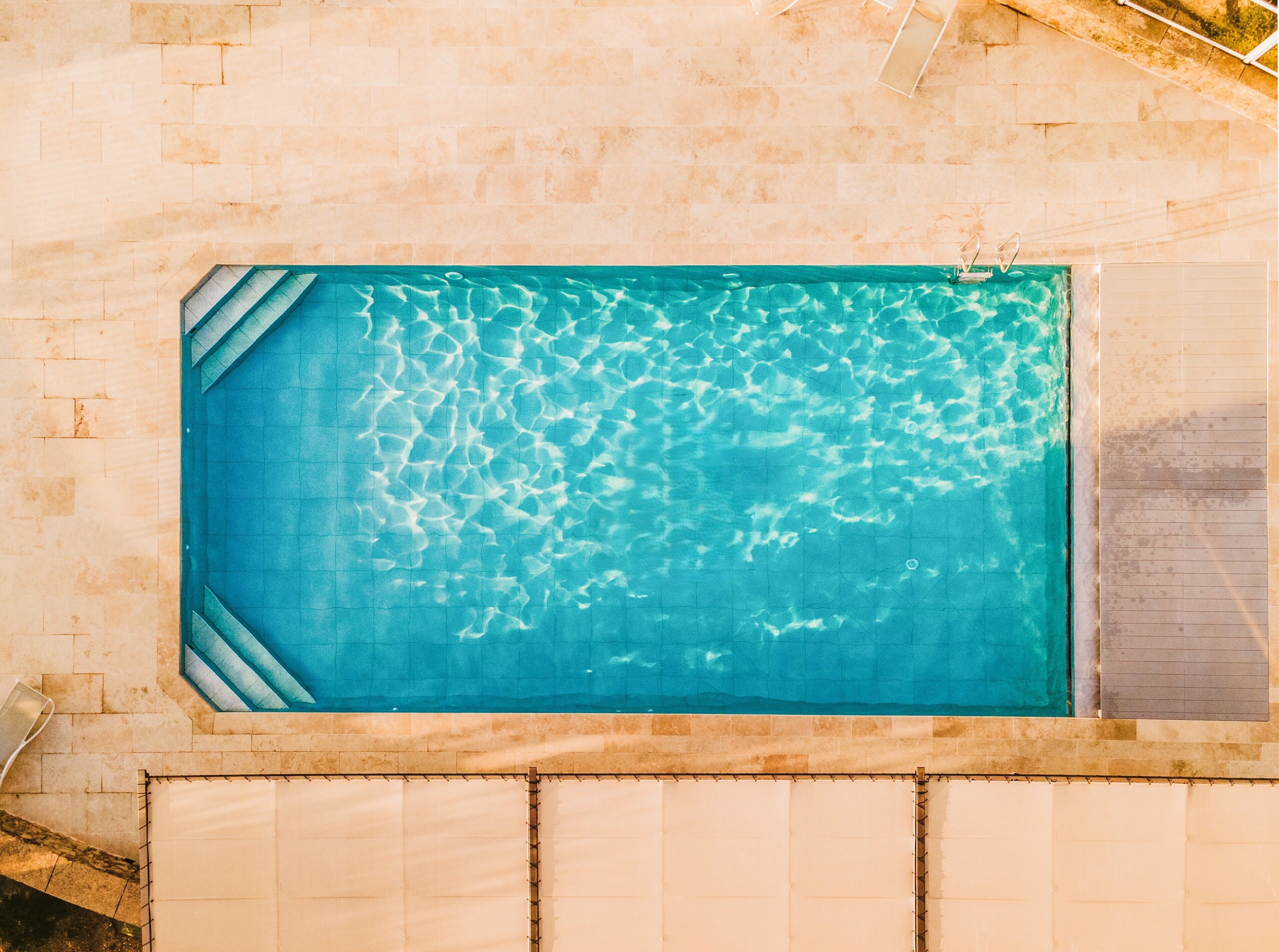 A rectangular swimming pool with clear water, surrounded by light-colored tiled walls and a covered area with a metal frame.